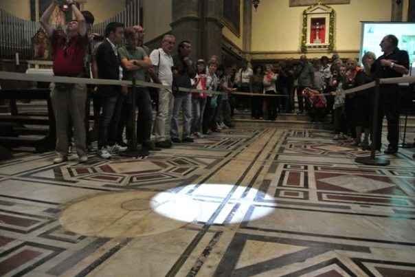 Cerchio di luce si sovrappone al marmo solstiziale sotto lo sguardo dei turisti